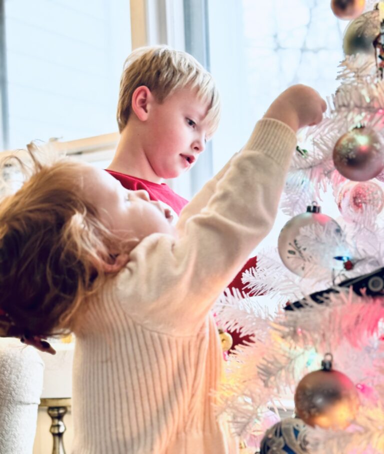 two kids hanging ornaments on a white christmas tree