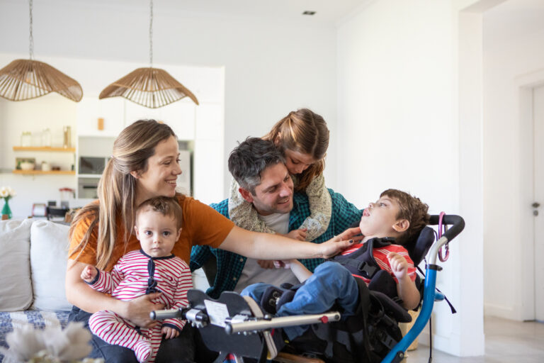 A loving family gathered in their living room, with parents and siblings interacting joyfully, including a child in a wheelchair.